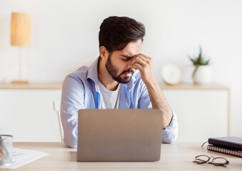 Desperate Eastern Freelancer Guy Sitting At Desk With Laptop, Suffering Lack Of Inspiration Or...