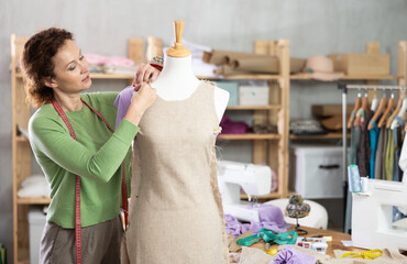 Woman tailor connects parts of dress on mannequin. Craftsman attaches front part of dress to back...