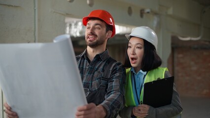 Multinational happy engineers construction teamwork site inspection blueprint discussion success safety progress planning diverse workers business Asian woman Caucasian man building project analysis