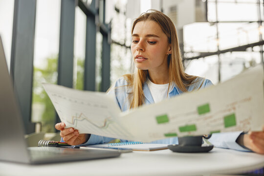 A dedicated and focused woman meticulously examines various business charts while working at a contemporary desk