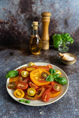 Close up front view of assorted sliced tomatoes, basil leaves, olive oil bottle and pepper mill on...