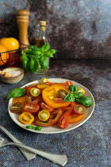 Front view of mixed tomatoes, fresh basil, olive oil bottle and wooden pepper mill on dark blue...