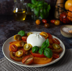 Close up of burrata with sliced and cherry tomatoes, basil leaves, olive oil and bowl of sea salt...