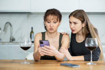 Two distressed friends read news on phone during gatherings, discuss unexpected changes. Woman, while treating friend, shows unpleasant news on phone, distressing photo and complains about bad news