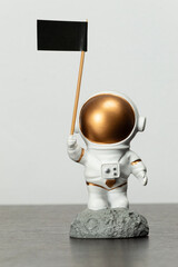 an astronaut toy over a dark brown wooden table with a black flag in its right hand and white...