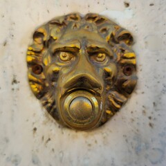 Decorative brass doorbell in the shape of a lion's head mounted on a stone wall in Rome, Italy....