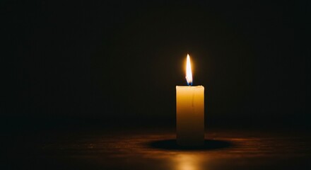 A solitary burning candle provides a warm glowing light in the darkness, representing a spiritual concept of memory, remembrance, and quiet contemplation.