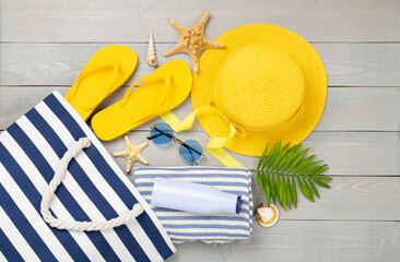 Blue beach bag with summer accessories on wooden background, top view