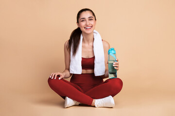 Healthy beautiful smiling young woman in sportswear and white towel on neck sitting on the floor...
