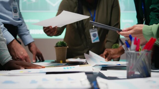 After hours briefing with multiethnic group gathering in a strategy room, analyzing visual data, statistics and risk assessment files for project development, productivity. Camera A.