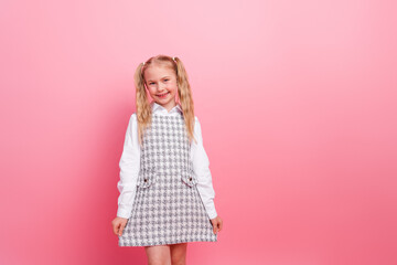 Adorable little schoolgirl in a formal uniform smiling against a pink background, symbolizing childhood learning and education