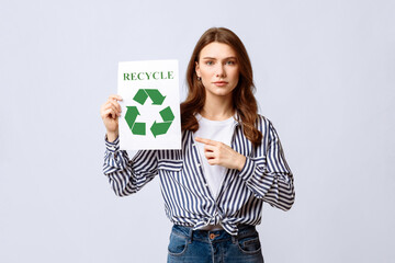 A woman holds a recycling sign, emphasizing the importance of eco-friendly habits. She is dressed casually and engages viewers in a sustainable conversation, likely in an indoor environment.