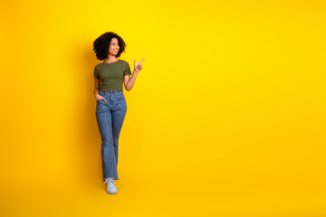 Confident young woman pointing towards empty yellow background, stylish in casual outfit with charming smile