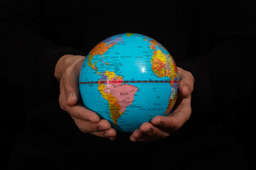 a male hands holding an earth globe with political south america map and black background