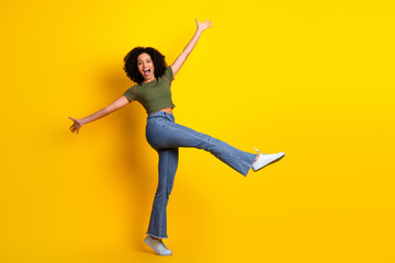 Joyful young woman in casual green attire and jeans posing energetically with a radiant smile on a vibrant yellow background
