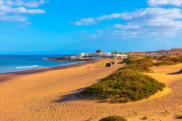Sunny beach of Playa Blanca in Fuerteventura, Canary Islands. Sand dunes meet the ocean, creating a beautiful natural landscape. Ocean waves gently roll onto sandy beach, a picturesque coastal view