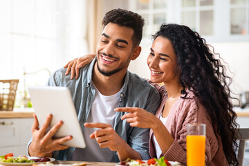 Cheerful Middle Eastern Spouses Using Digital Tablet While Having Breakfast In Kitchen At Home,...
