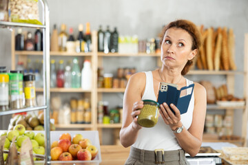 Adult female shopper scanning qr code for green peas in jar in grocery store