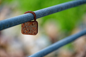 Severely rusted padlock hanging on metal bar with flaking rust