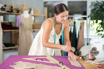 Woman seamstress prepares to cut out details, attaches paper pattern to fabric. Clothing design,...