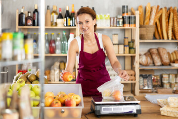 Adult female seller weighing apples in plastic bag in grocery store