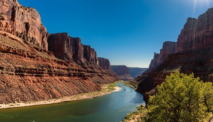 deep canyon with a winding river at the bottom and towering rock walls on either side under a clear sky with the sunlight casting deep shadows