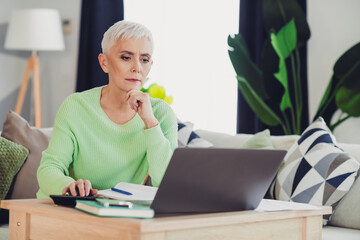 Mature woman using a laptop at home relaxing on a couch. Senior adult working or browsing online in...