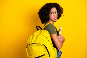 Stylish teenage girl wearing a yellow backpack and glasses making a funny face against vibrant yellow background