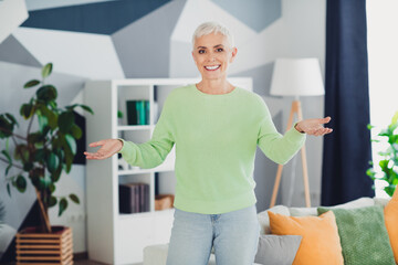 Mature woman with a charming smile in a stylish sweater enjoying relaxing time in a comfortable...