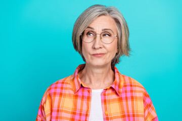 Charming elderly woman with a vibrant checkered shirt against a turquoise backdrop exuding...