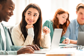 Obraz premium Young black man and latin woman working together in public library or office. Group of students studying together in classroom, excited lady pointing at laptop screen, people discussing research