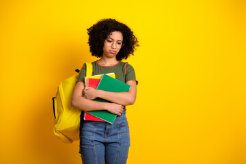 Young female student holding colorful notebooks standing against vibrant yellow background with casual style and posture