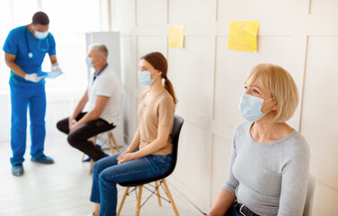 Mature woman and other patients in face masks waiting in queue for vaccination against covid-19 at...