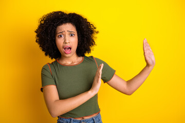 Young woman with curly hair gesturing in surprise and alarm on a vibrant yellow background