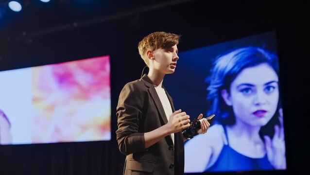 Young Caucasian Male Presenter Speaking on Stage at Conference with Modern Screens
