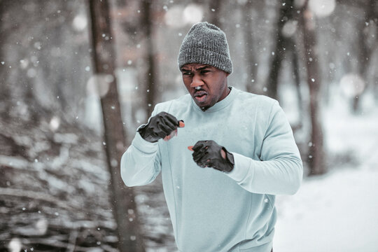 Focused Black man shadowboxing in snowy forest during winter outdoor workout