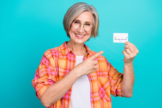 Smiling mature woman holding a credit card and pointing with a gesture for advertising on a teal background