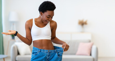 New Size. Excited Slim African Woman Wearing Old Oversized Pants After Successful Weight Loss...