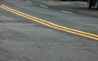 Yellow Lines on a Winding Road. Abstract turning road background with tires track and yellow striped road marking on dark asphalt.	
