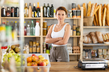 Portrait of positive female salesperson behind supermarket counter. Interior of a grocery...