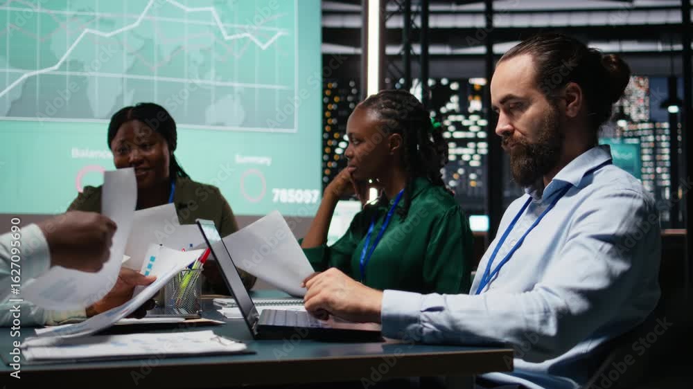 Poster diverse team of analysts reviewing annual data reports in after hours meeting, developing internal c