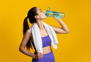 Sports Hydration. Portrait of fit young woman with white towel on neck drinking fresh water from...