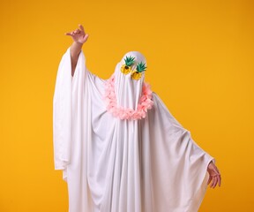 Funny ghost. Man covered with white sheet in sunglasses and wreath of flowers dancing on orange...