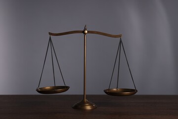 Scales of justice on wooden table against grey background