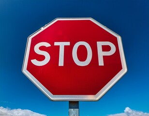 Obraz premium a bright red octagonal stop sign with white lettering and a reflective surface stands alone against a clear blue sky with a few wispy clouds
