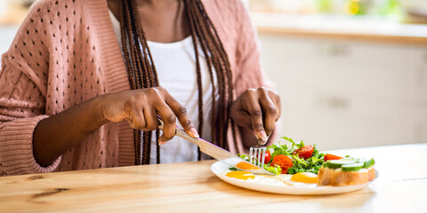 Morning Meal. Cropped Image Of Young Black Woman Eating Breakfast In Kitchen, Unrecognizable African American Lady Sitting At Table And Enjoying Tasty Food, Using Fork And Knife, Cropped Shot