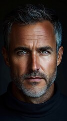Obraz premium Close-up portrait of a mature man with gray hair and beard, intense eyes, and serious expression wearing a dark turtleneck against a dark background