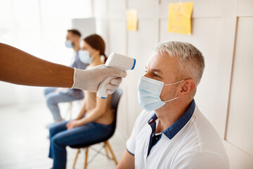 Senior man in medical mask waiting for covid-19 vaccination at hospital, doctor checking his...