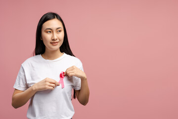 Asian woman attaching pink ribbon to white t-shirt for breast cancer awareness