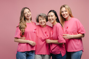 Diverse women embracing and showing pink ribbons for breast cancer awareness